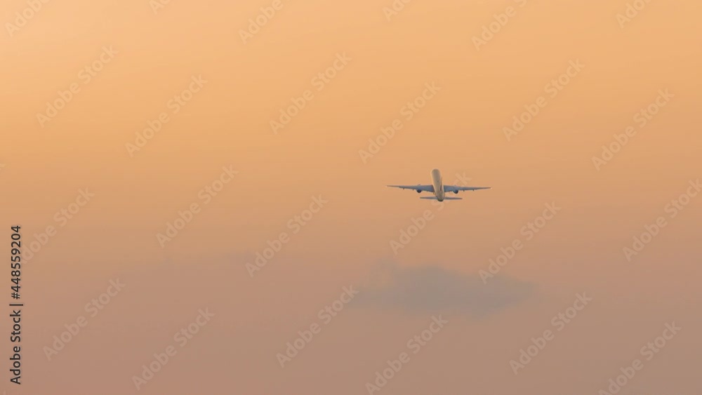 Airplane flies high in the air against orange sky. Sunset or sunrise colors. Aircraft ascending and travelling away. Slow motion view of large passenger plane above Airplane flies high in the air against orange sky. Sunset or sunrise colors. Aircraft ascending and travelling away. Slow motion view of large passenger plane above