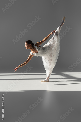 Fototapeta Naklejka Na Ścianę i Meble -  Side view of ballerina standing on one leg on grey background