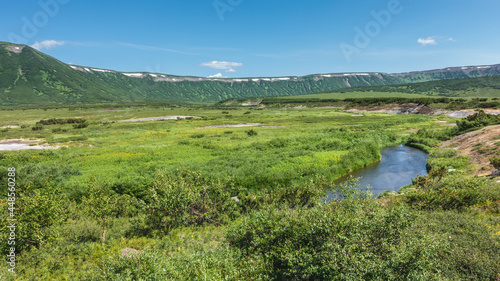 The caldera of an extinct volcano is surrounded by a ridge. There is a green meadow and a lake in the valley. Clear blue sky. A sunny summer day. Kamchatka. Uzon