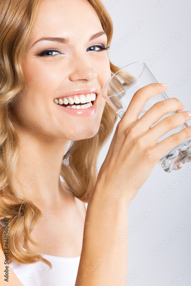 Portrait photo of young happy smiling woman drinking water, isolated over gray background. Attractive blond girl at studio. Portrait photo of young happy smiling woman drinking water, isolated over gray background. Attractive blond girl at studio.