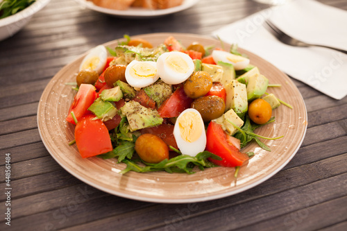 dish of fresh vegetables arugula, avocado, cherry tomatoes with olives and quail eggs on dining table