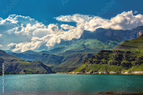 Toned mountain landscape view with turquoise lake. Summer cloudy day. Cucasus scene with green high hills, body of blue water and deep sky.