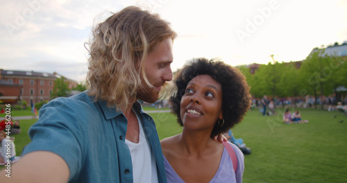 Happy young diverse couple taking selfie or having video call in park