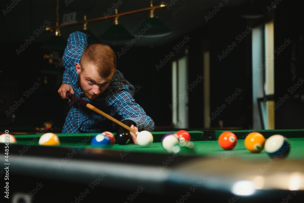 Fototapeta premium Young man playing billiards in the dark billiard club