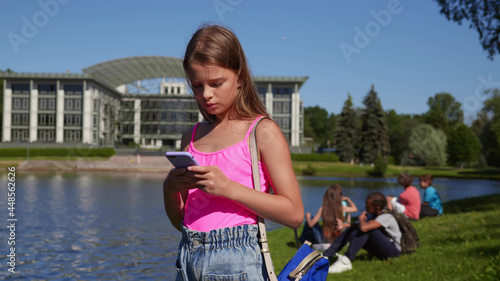 Caucasian pre-teen girl using mobile phone standing in summer park photo