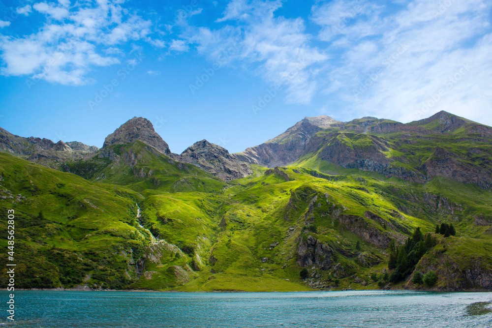 Mountain lake in the middle of the alps. Summer in the green mountain with a blue lake. Alpine mountains with a play of light and shadow of the clouds.