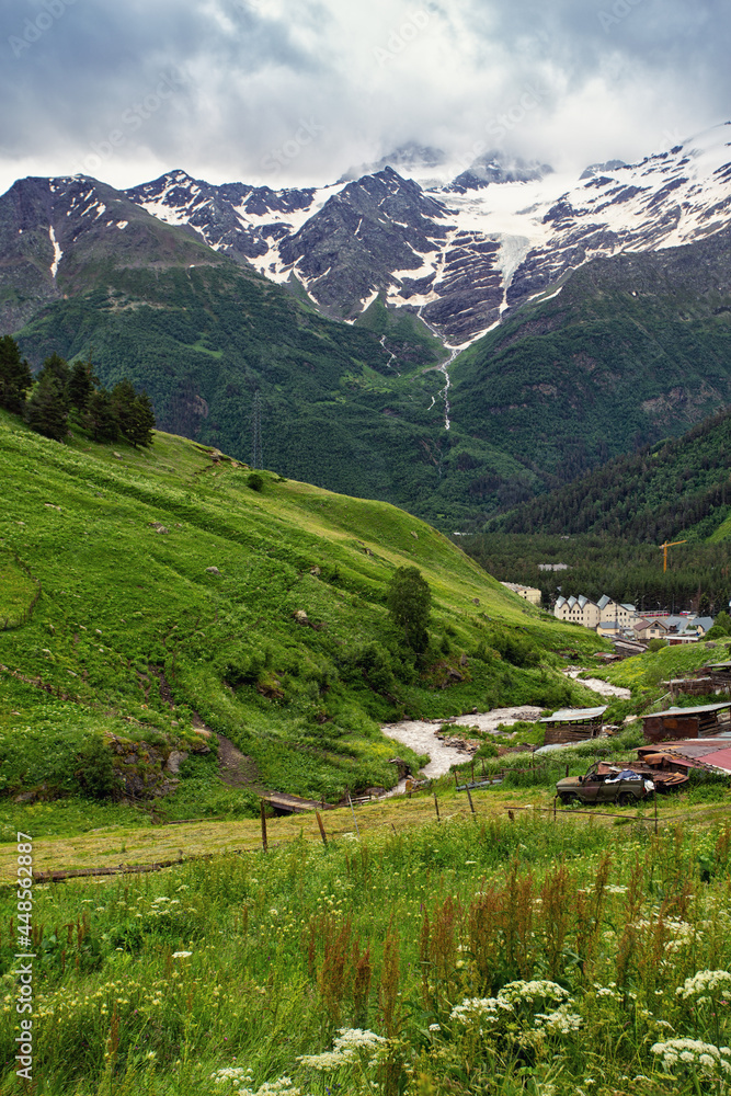 Picturesque green valley among high mountains and gray cloudy sky in Caucasus. Vertical beautiful landscape outdoors.