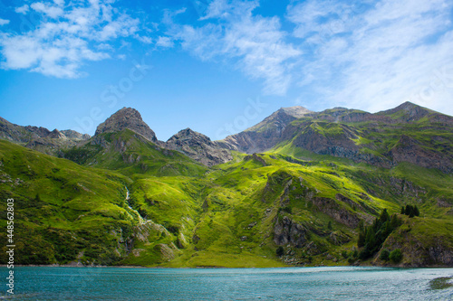 Mountain lake in the middle of the alps. Summer in the green mountain with a blue lake. Alpine mountains with a play of light and shadow of the clouds. © Tilcara