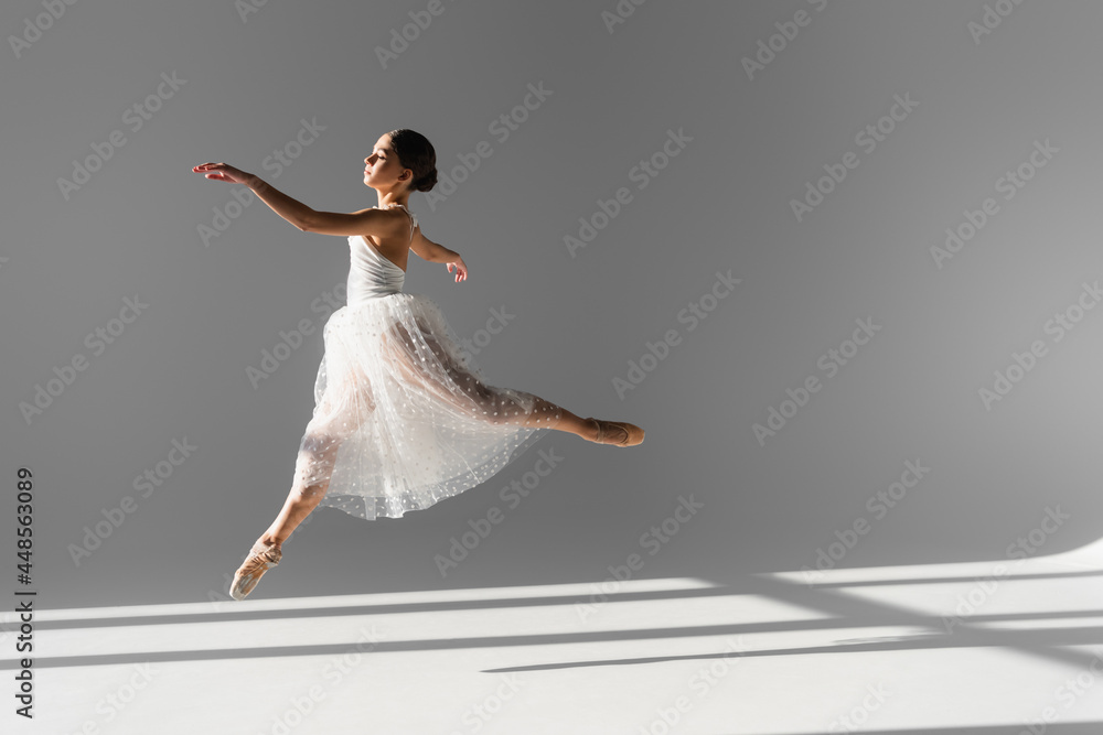 Side view of professional ballerina jumping on grey background with sunlight Side view of professional ballerina jumping on grey background with sunlight