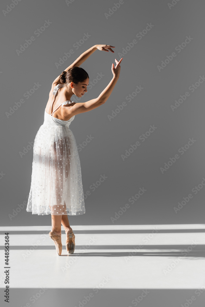 Naklejka premium Side view of ballerina bending and looking down on grey background with sunlight
