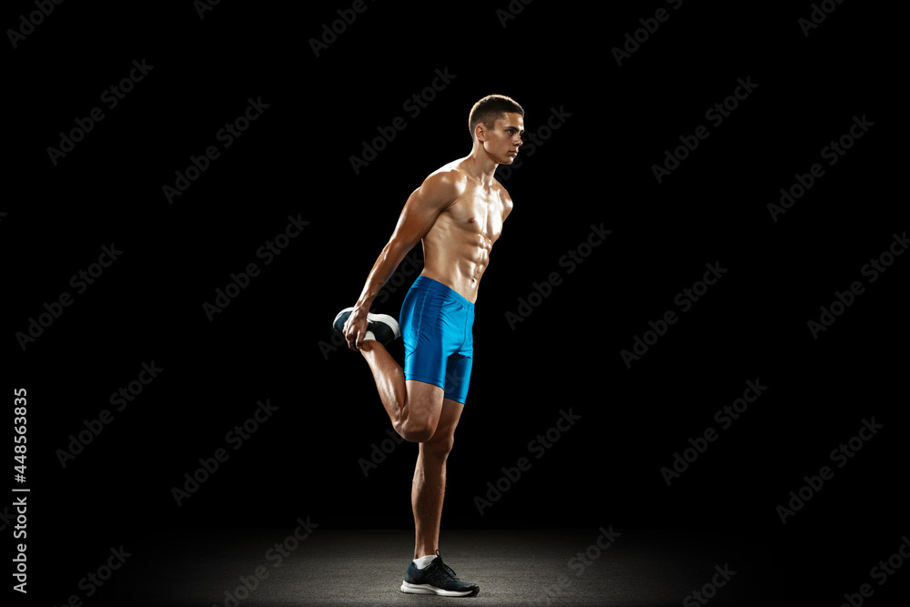 Warm-ups. Young male athlete, runner practicing isolated on black studio background. Muscular, sportive man. Concept of sport, healthy lifestyle