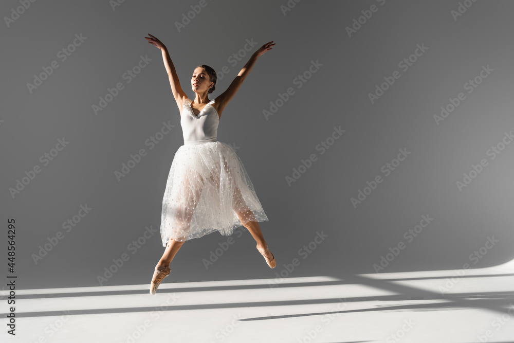 Young ballerina dancing and jumping on grey background with sunlight Young ballerina dancing and jumping on grey background with sunlight
