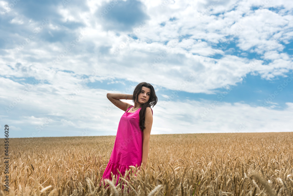 Beautiful model in fashionable dressed walks across a field of mature wheat Beautiful model in fashionable dressed walks across a field of mature wheat