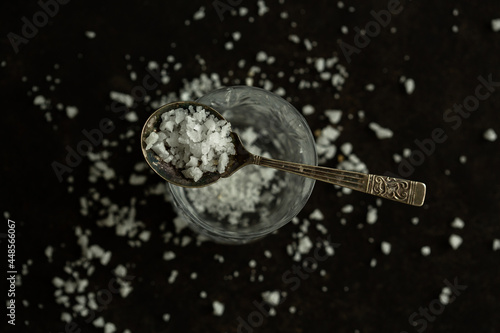 Salt, pure sea salt with no additives. Coarse white salt on dark black background with a spoon.