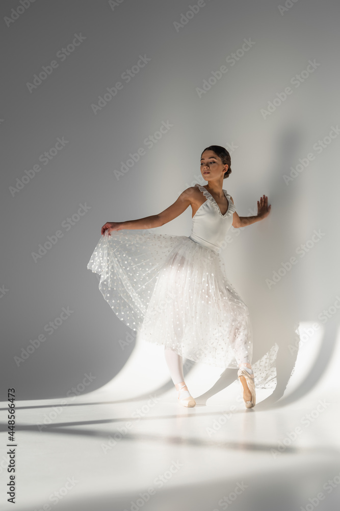Naklejka premium Professional ballerina holding skirt on grey background with shadow
