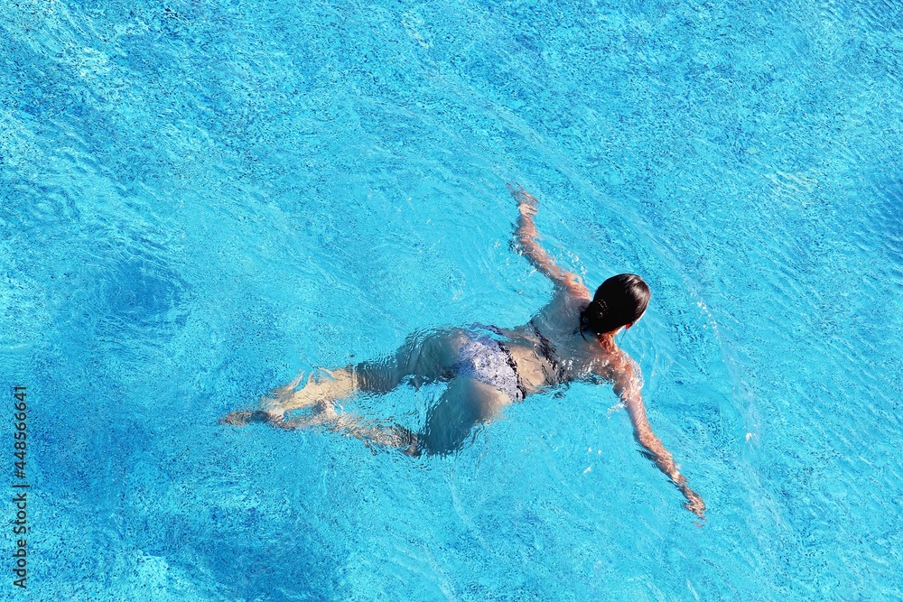 Girl in a swimsuit swimming in the pool water, top view. Water sports, beach vacation
