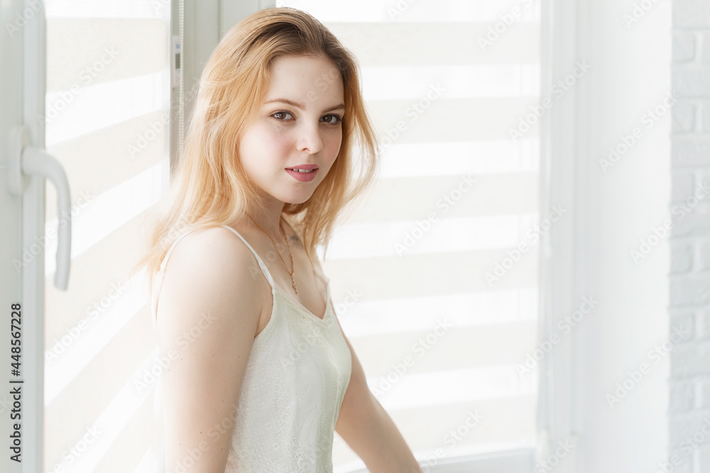 beautiful young woman sitting by the window in a white room beautiful young woman sitting by the window in a white room