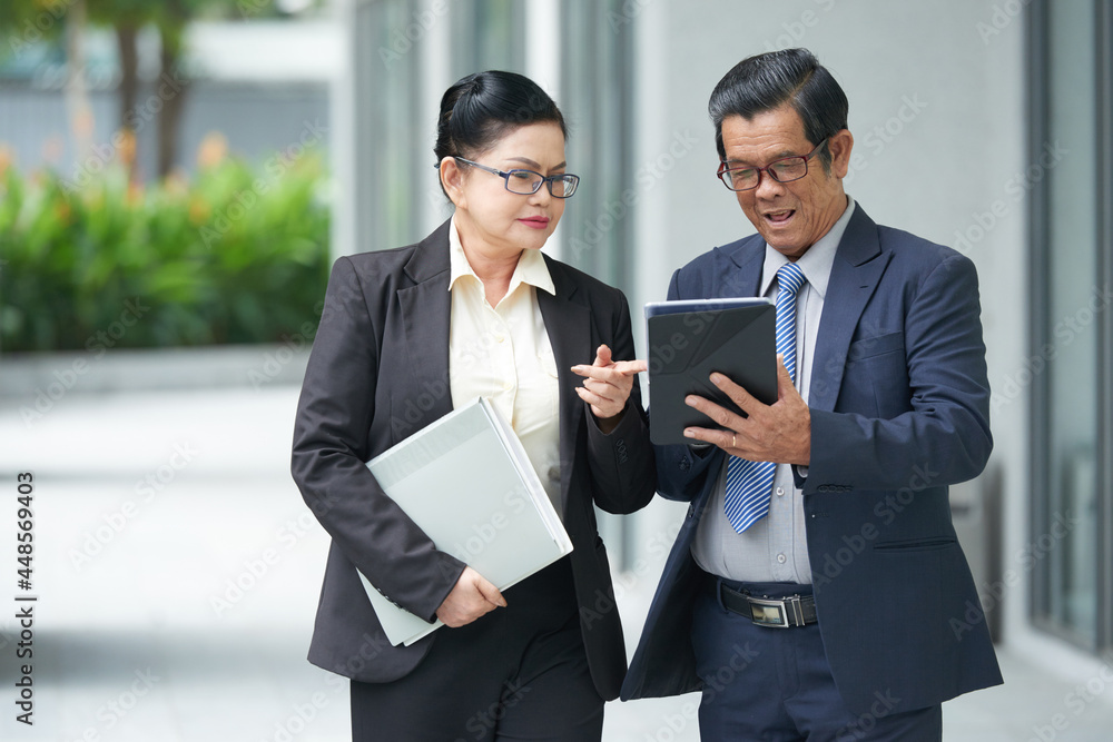 Senior business couple discussing information on tablet computer when having meeting outdoors Senior business couple discussing information on tablet computer when having meeting outdoors