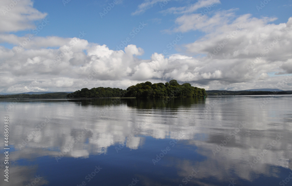 Fototapeta premium Reflection of an island in a lake with clouds on the horizon