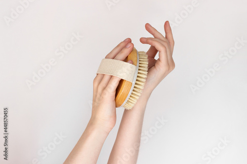 Hand is holding hatural wooden body brush in front of white background. Woman scrubbing her hand. Massage, relax, spa. eco-friendly, zero waste product. Beauty, skincare, wellness concept