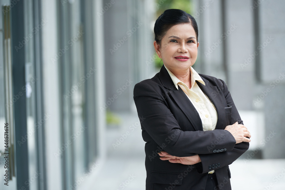 Portrait of confident smiling senior female entrepreneur standing outdoors with arms crossed and looking at camera Portrait of confident smiling senior female entrepreneur standing outdoors with arms crossed and looking at camera