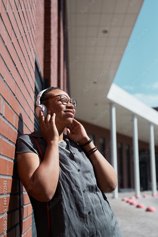 Fototapeta premium African happy woman in wireless headphones listening to music and enjoying the sunny weather outdoors