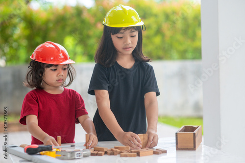Asian Siblings girls wearing engineering hats building House from the wooden toy. To learning and enhance development  little architect.