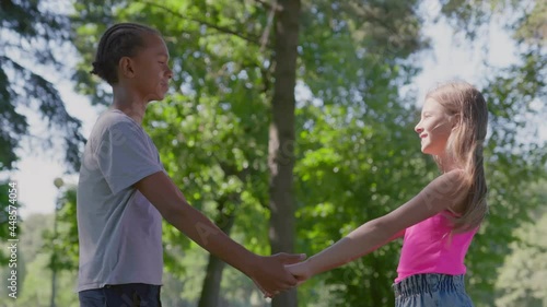 Side view of caucasiangirl and african boy hold hands standing together in park photo