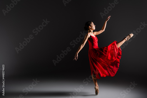 Side view of ballerina dancing one one leg on black background