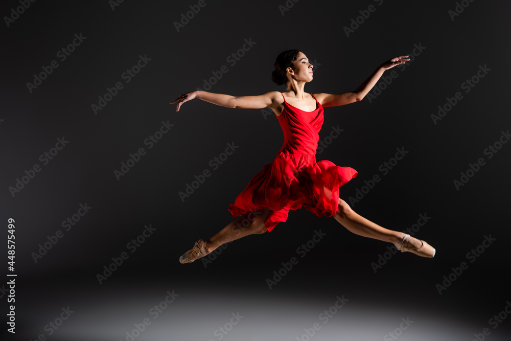 Side view of ballerina in red dress jumping on black background Side view of ballerina in red dress jumping on black background