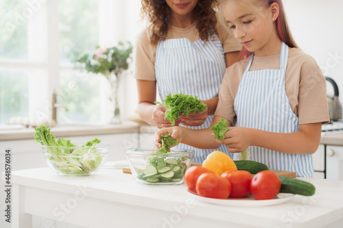 Mother and teen daughter preparing vegetable salad at kitchen