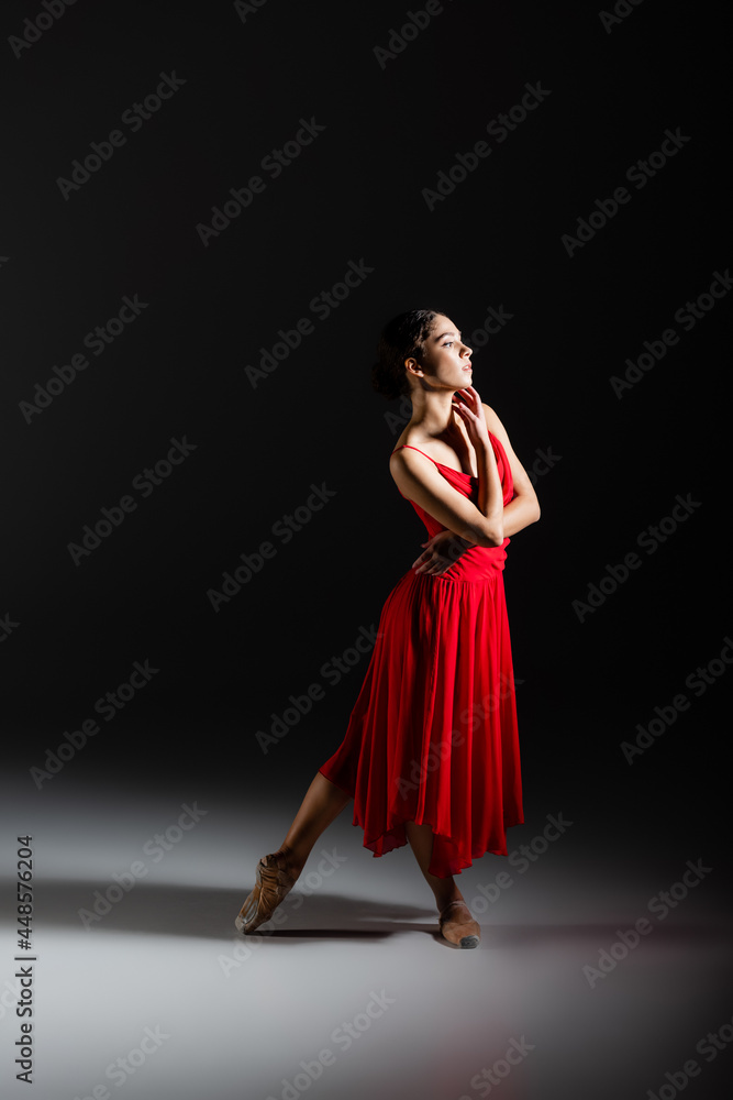 Side view of classical dancer in pointe shoes standing on black background