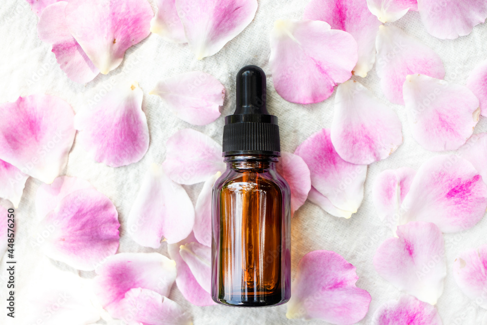 Glass dropper bottle and rose petals on a white background. Top view, place for text. Glass dropper bottle and rose petals on a white background. Top view, place for text.