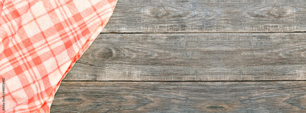 Folded checkered red and white tablecloth on a rustic brown wooden kitchen table top view. Summer picnic product display montage template, banner. Folded checkered red and white tablecloth on a rustic brown wooden kitchen table top view. Summer picnic product display montage template, banner.