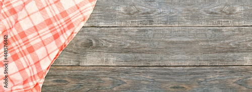 Folded checkered red and white tablecloth on a rustic brown wooden kitchen table top view. Summer picnic product display montage template, banner.
