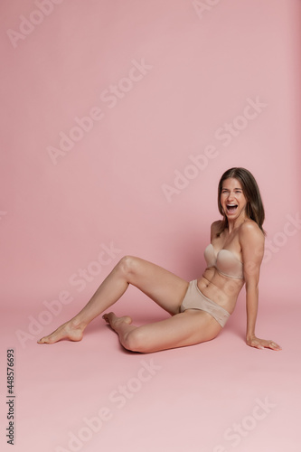 Portrait of young beautiful tanned woman in lingerie posing isolated over pink studio background. Natural beauty concept.