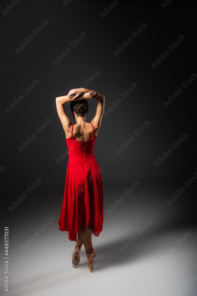 Back view of ballerina in red dress and pointe shoes standing on black background