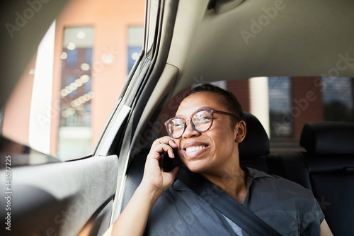 African happy woman in eyeglasses talking on mobile phone during her ride in the car