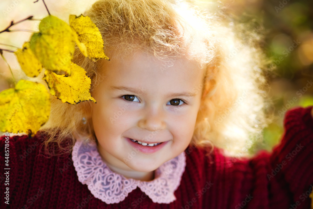 A child in an autumn park flooded with the sun. A little blonde girl in a bard knitted sweater among yellow leaves A child in an autumn park flooded with the sun. A little blonde girl in a bard knitted sweater among yellow leaves