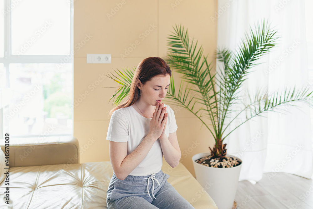 Closeup portrait of a young woman praying sincerely with folded arms at home or indoors. Sincere prayer of a Caucasian girl or female in the church with closed eyes alone. close up at home in the room Closeup portrait of a young woman praying sincerely with folded arms at home or indoors. Sincere prayer of a Caucasian girl or female in the church with closed eyes alone. close up at home in the room