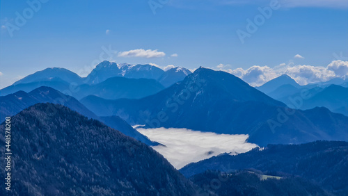 A panoramic view from the top of Alpine peak in Austria. The whole area is shrouded in thick clouds. A few peaks popping out from the clouds. High mountain chains in the back. Carpet from the clouds © Chris