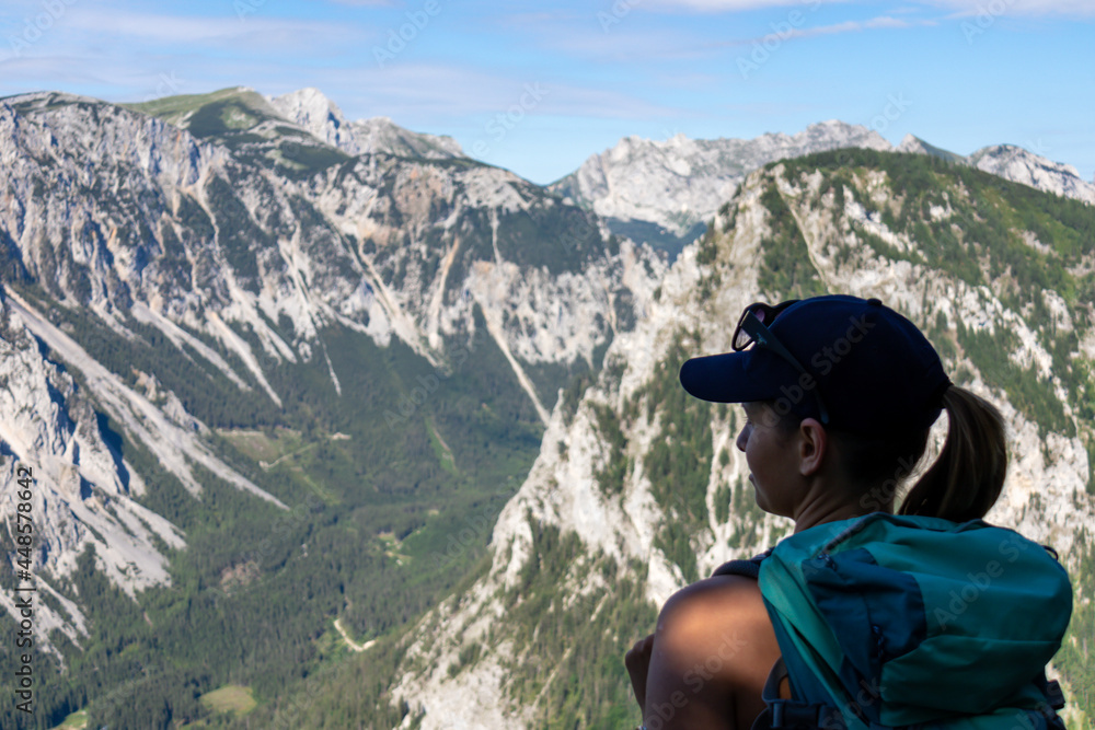 A woman with a hiking backpack admiring the view on the Alpine mountain chains in Austria, Hochschwab region. The slopes are partially overgrown with small bushes, higher parts baren. Happiness