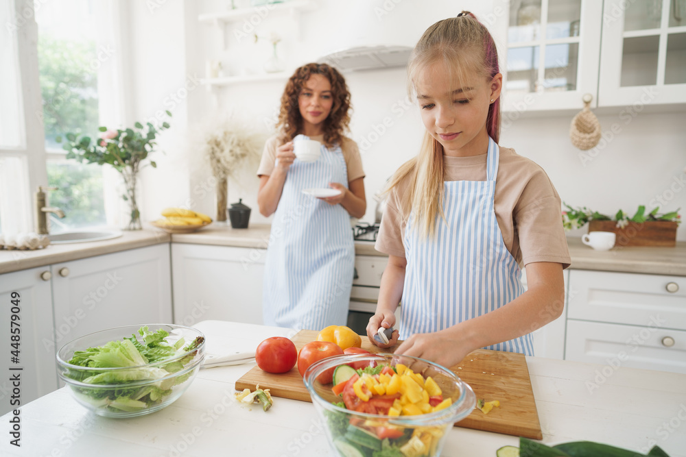 Mommy teaching her teen daughter to cook vegetable salad in kitchen