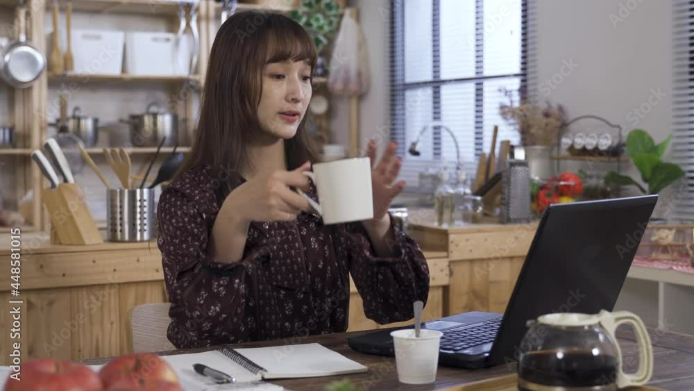 asian businesswoman is taking a break to ponder by sipping the coffee while working from home with her laptop in the home dining room. asian businesswoman is taking a break to ponder by sipping the coffee while working from home with her laptop in the home dining room.