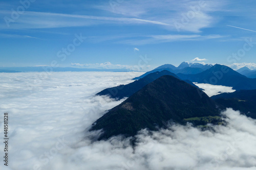 A panoramic view from the top of Alpine peak in Austria. The whole area is shrouded in thick clouds. A few peaks popping out from the clouds. High mountain chains in the back. Carpet from the clouds © Chris