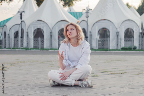 A beautiful woman in white clothes is sitting on a concrete tile on the street