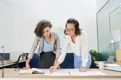 Foto Serious businesswomen bending over table with charts and reports and analyzing f