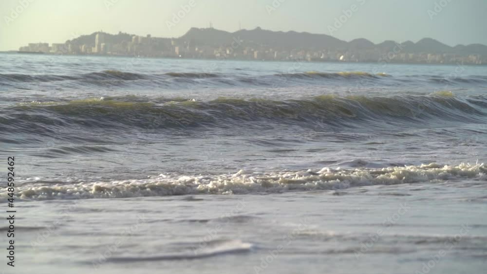 Seascape at sunset with long sea waves and coastal town on background. Seascape at sunset with long sea waves and coastal town on background.
