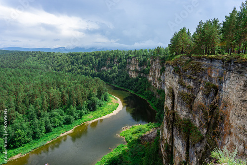 A river in a mountain gorge, aerial view, filmed from a drone. River at the foot of a stone cliff. The coast is covered with forest. View of the mountain gorge.