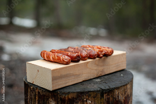 Grilled sausages lie on a wooden board on a stump.
